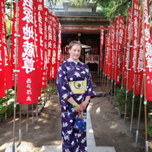 Teri wearing a violet kimono standing in front of red flags