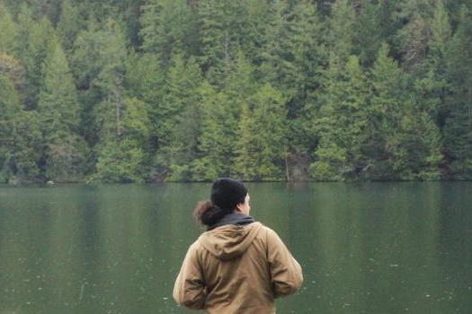 在户外静修中，一名学生望着被常青树环绕的湖泊，沉思着.