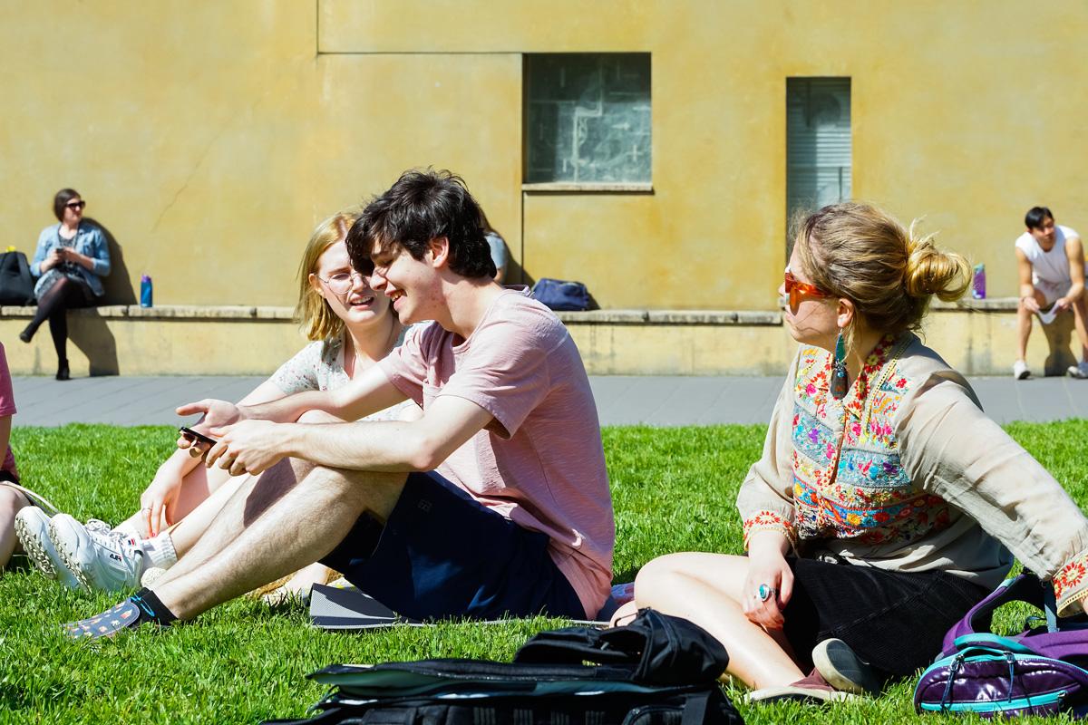 一群穿着短裤和运动鞋的学生在绿色的草坪上晒太阳，其他人则靠在教堂的墙上